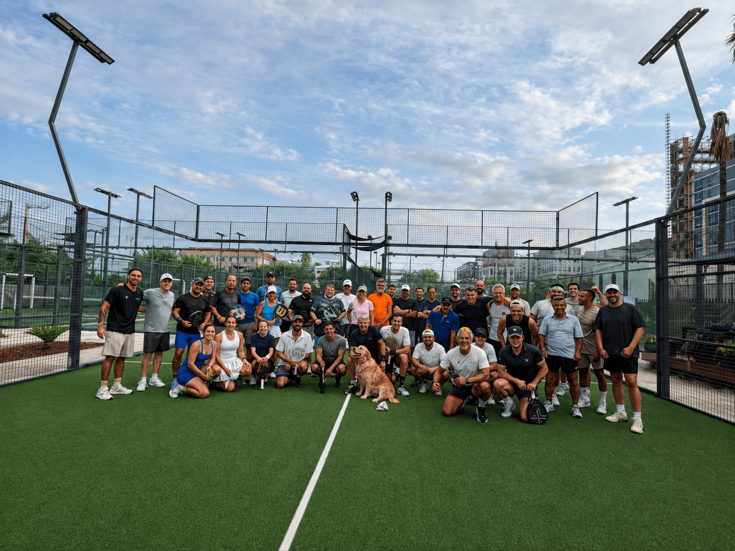 A large group of club members posing on court with a golden retriever