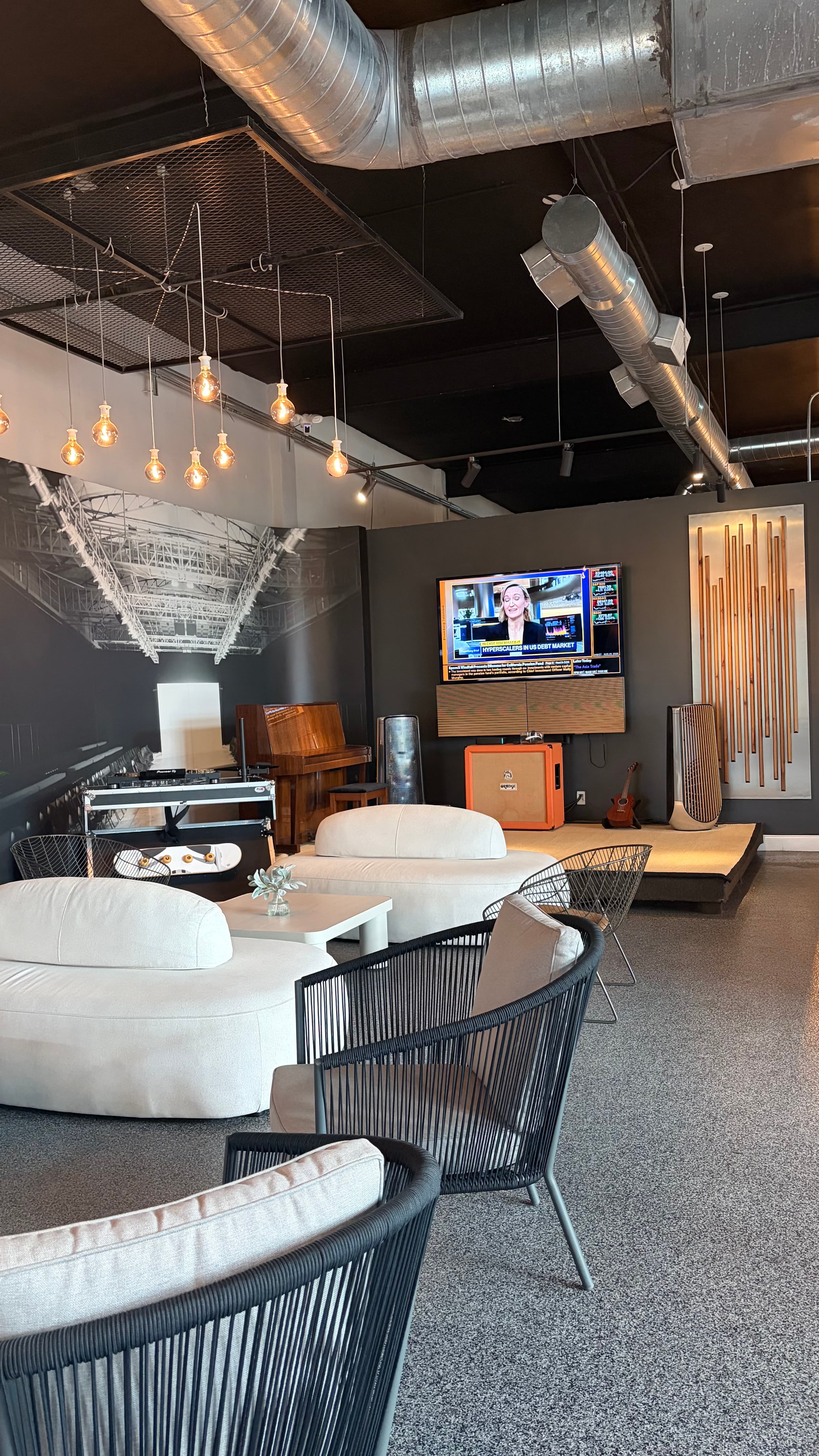 Lounge seating area with cream sofas, black rope chairs, a piano and DJ booth, and a wall-mounted TV